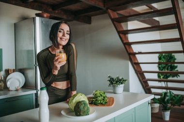 Mutfakta sağlıklı yiyeceklerle poz veren güzel ve sportif bir kadın.