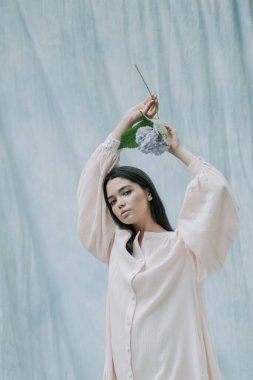 Ortanca çiçekleriyle kumaş arka planda poz veren hoş genç bir kadın. 