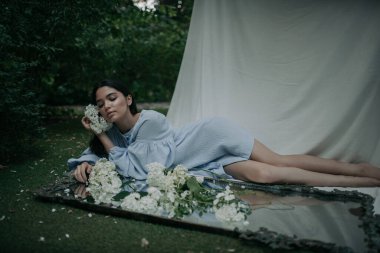 Parkta çiçeklerle poz veren güzel bir genç kadının portresi.