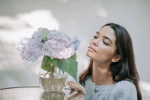 Süslü cam masadaki vazoda ortanca çiçeklerine dokunan kız.  