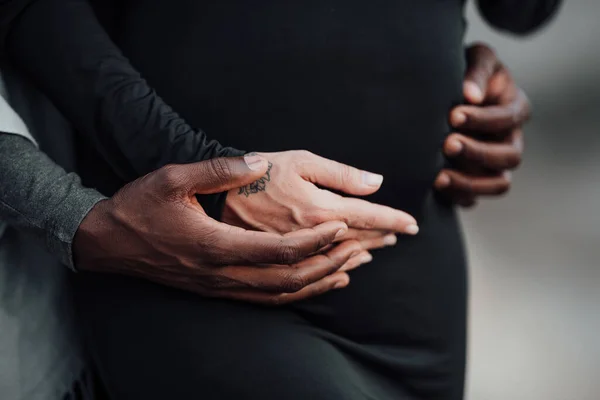 african american man holding hands on belly of pregnant woman in black dress