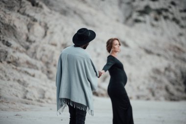 Granit kanyona karşı poz veren çok ırklı bir çift. Siyah bir elbise giyen hamile bir kadın. 