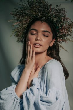 Çelenk takmış çekici bir kadının portresi elleriyle yüzüne dokunuyor.