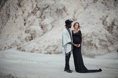 Granit kanyona karşı poz veren çok ırklı bir çift. Siyah bir elbise giyen hamile bir kadın. 