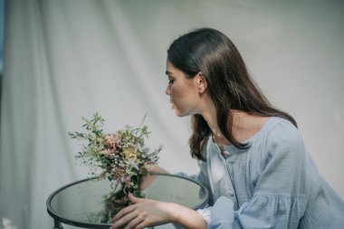 Dekoratif cam masa ve çiçeklerle poz veren kız 