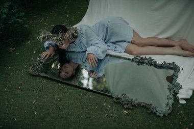 Çiçekli çelenk giymiş çekici bir kadın parktaki aynaya bakıyor.