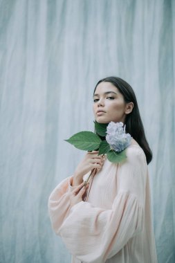 Kumaş arka planda ortanca çiçekleriyle poz veren hassas kadın portresi 