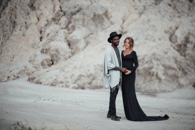 Granit kanyona karşı poz veren çok ırklı bir çift. Siyah bir elbise giyen hamile bir kadın. 