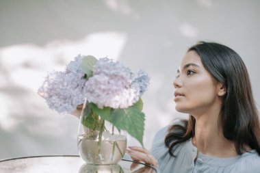 Süslü cam masadaki vazoda ortanca çiçeklerine dokunan kız. 