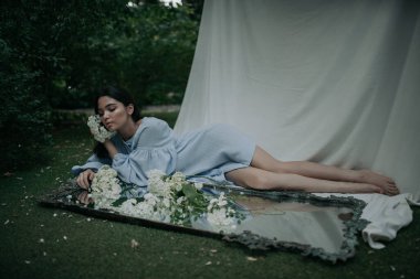 Parkta çiçeklerle poz veren güzel bir genç kadının portresi.