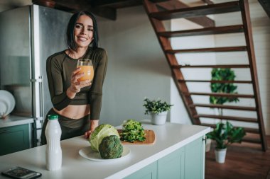 Mutfakta sağlıklı yiyeceklerle poz veren güzel ve sportif bir kadın.