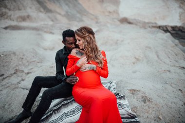  Granit kanyona karşı poz veren çok ırklı bir çift. Şık kırmızı elbise giyen hamile bir kadın. 