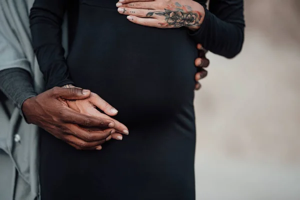 african american man holding hands on belly of pregnant woman in black dress