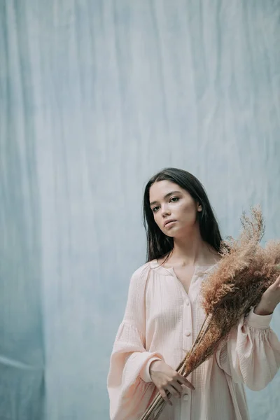 黑发女人 身穿粉色衣服 背对着布料背景 摆着干枯的花朵 — 图库照片