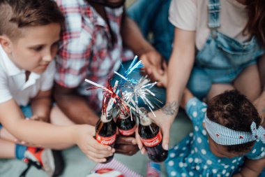 Parkta piknik yaparken yanında pipetli kola şişeleri olan kırpılmış bir aile. 