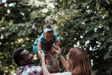 Mutlu aile gündüz vakti yaz parkında tatlı bir kızla oynuyor.
