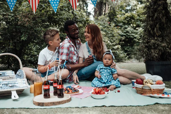 夏の公園でピクニックで家族を祝う 幸せな両親は昼間は小さな子供と果物やケーキを食べています — ストック写真