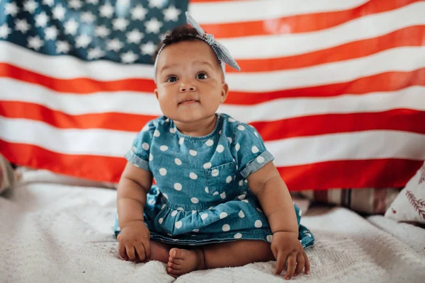 Mavi elbiseli sevimli küçük kız Amerikan bayrağıyla kanepede oturuyor.  