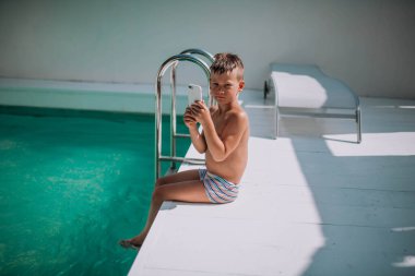 Genç çocuk yazın yüzme havuzunun yanında oturuyor.