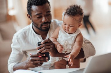 İş adamı kızını kucağında tutarken bilgisayarla evden çalışıyor.