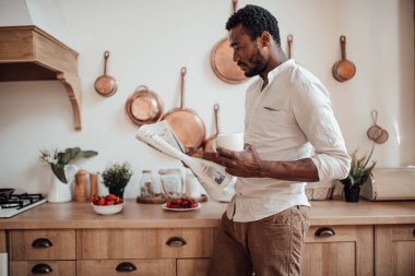 Afro-Amerikan gömlekli adam gazete okuyor ve kahve içiyor.
