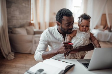 İş adamı kızını kucağında tutarken bilgisayarla evden çalışıyor.