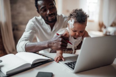 İş adamı kızını kucağında tutarken bilgisayarla evden çalışıyor.