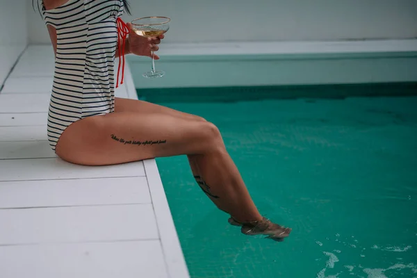 partial view of young woman with cocktail nearby pool