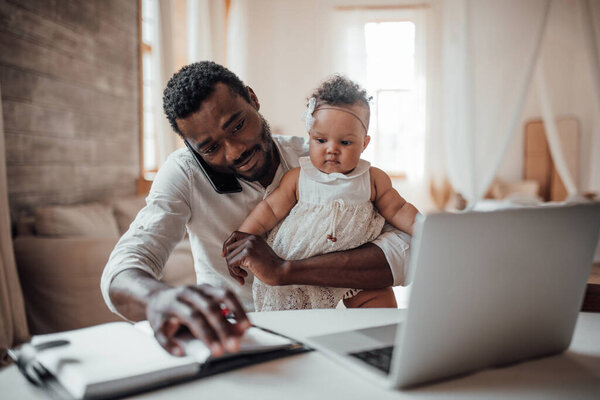 businessman working from home on laptop while holding daughter