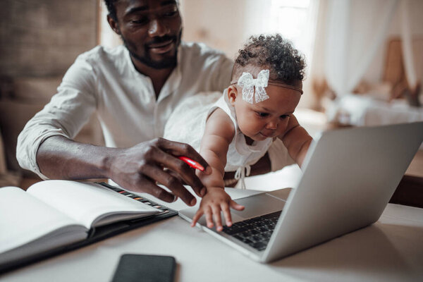 businessman working from home on laptop while holding daughter