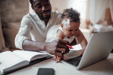 Kızı kucağında tutarken evden bilgisayarla çalışan Afrikalı iş adamı