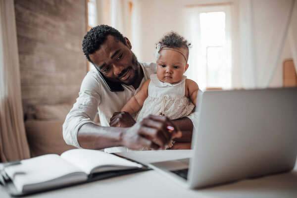 businessman working from home on laptop while holding daughter