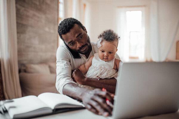 young african man working and holding little girl at home