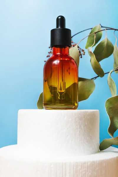 Mavi Arkaplanda Pipette Cam Şişeli Anti-Age Yüz Serumu. Yeşil okaliptüs yapraklı kozmetik esansı yağı. Podyumda yüz bakımı antioksidan, C vitamini, Retinol tedavisi