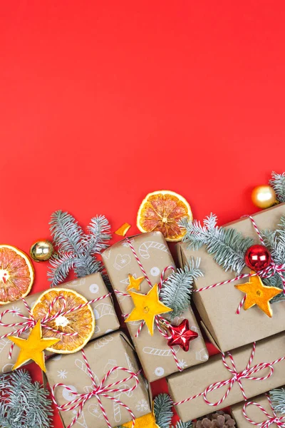Many craft gift boxes on red background. Christmas holiday package wallpaper with christmas tree branch, dry orange slices, balls above. Handmade wrapped paper. New year knolling flat lay, copy space