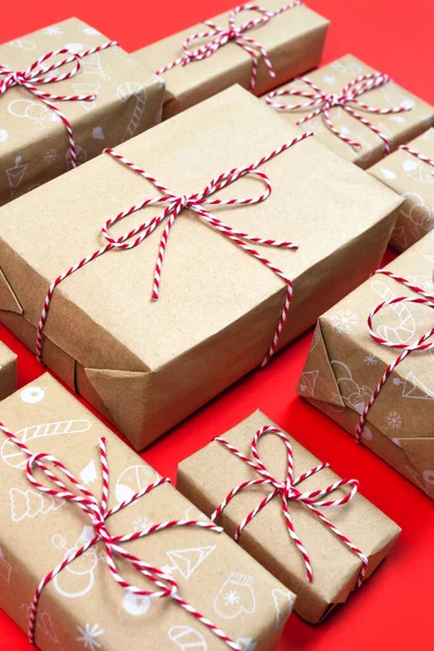 Many handcraft gift boxes on red background. Christmas season holiday packaging minimal ornament pattern. Trendy present diy. Handmade parcel wrapped striped rope and vintage paper. New year wallpaper