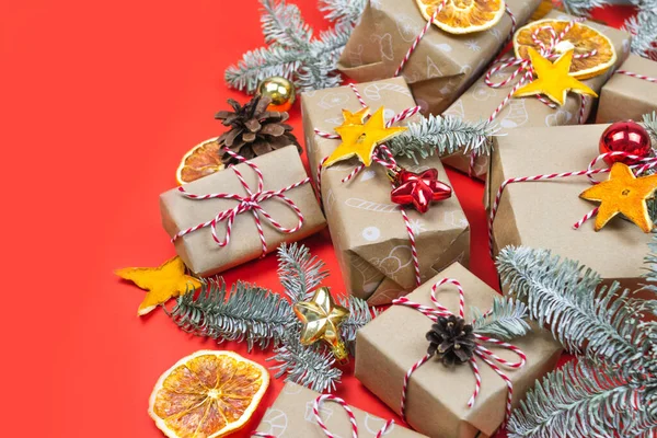 Many craft gift boxes on red background. Christmas holiday package banner template with copy space. Fir branch, dry orange slices, balls above. Handmade wrapped paper. New year zero waste still life