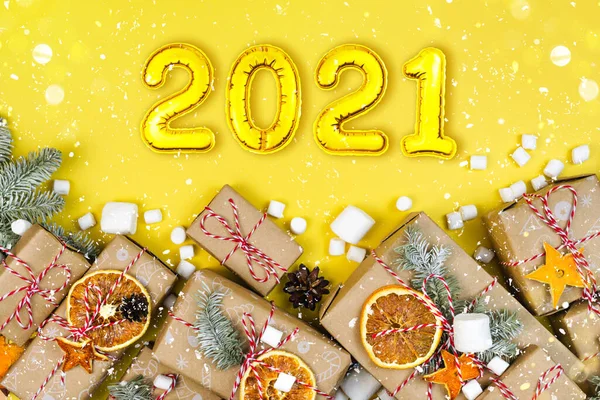 Many craft gift boxes on yellow background. 2021 New Year numbers, wrapped paper presents and garland light — Stock Photo, Image