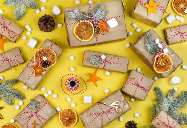 Sarı arka planda bir sürü ekolojik hediye kutusu var. Noel 'de Noel ağacı dallı duvar kağıdı paketleri, kuru meyve dilimleri, toplar. El yapımı kağıt kaplama. Yeni yıl hala hayat.