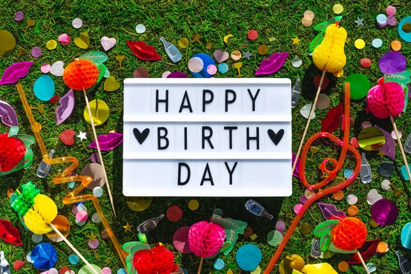Happy birthday greeting lightbox. Colorful party decor above on grass background. Holiday summer greeting concept. Natural green holiday top view wallpaper. Creative garden backyard celebrate vacation