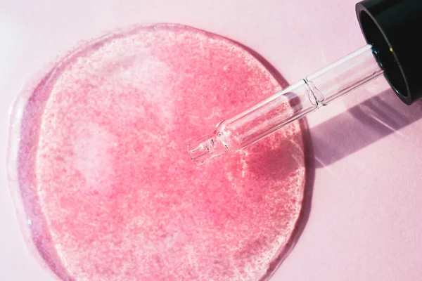 Pink serum, cosmetic fluid with pipette on bright background macro top view. Transparent beauty product with peptides, ceramides, hyaluron gel swatch texture. Glass dropper liquid makeup concept.