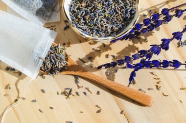 Ahşap masada kurutulmuş lavanta, kaşık ve çay poşeti. Organik bitkisel içecek. Sıfır atık paketi.