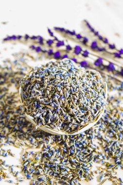 Ahşap masada kurutulmuş lavanta çiçekleri olan porselen bir kase. Organik bitki çayı içeceği. Temel şifalı aromatik bitki. Aromaterapi, ilaç, kuru kokulu malzeme. Sakinleştirici rahatlama içeceği