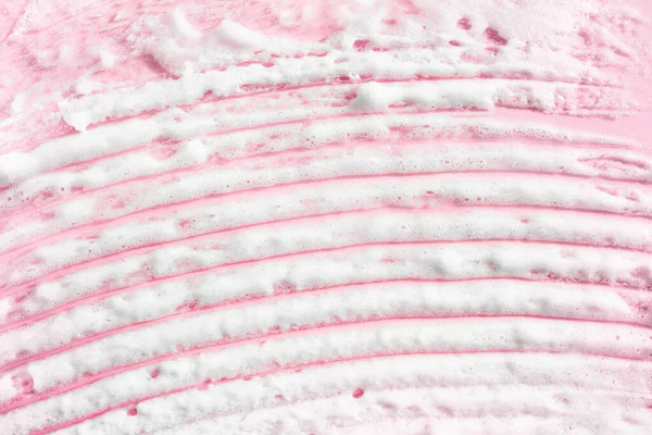 White smear of foam on pink background. Cosmetic of selfcare procedure. Beauty macro bubble texture wallpaper. Creme, shaving foam, mask, beauty product swatch closeup.