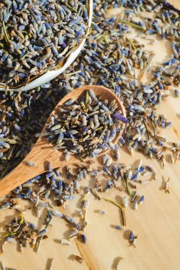 Tahta masadaki kaşık içinde kurutulmuş lavanta dolu porselen kâse. Organik sağlıklı bitkisel içecek. Güzellik kozmetiği ve parfüm malzemesi. İyileştirici aromatik bitki makro üst görünümü. Rahatlama içeceği