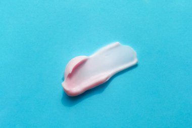 Parlak mavi arka planda izole edilmiş pembe kremalı köpük lekesi. Tıraş kremi, losyon, yüz maskesi, makyaj çıkarıcı. Face, vücut bakımı prosedürleri konsepti. Güzellik Bencillik Pankartı.