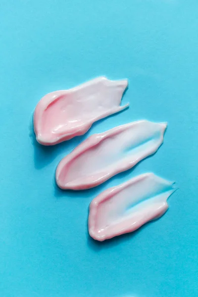 Ttree textured smears of pink creamy foam isolated on bright blue background. Shaving creme, lotion, facial mask, make-up cosmetic remover. Face, body care beauty products. Selfcare banner.