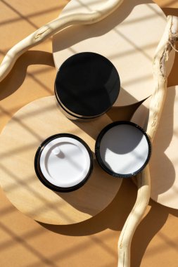 Ahşap kürsüde kozmetik krem cam kavanozlar, bej arka plan. Güzellik, kozmetik ürün reklamı için yuvarlak sahne kaidesi sunumu. Doğal organik düz konsept.