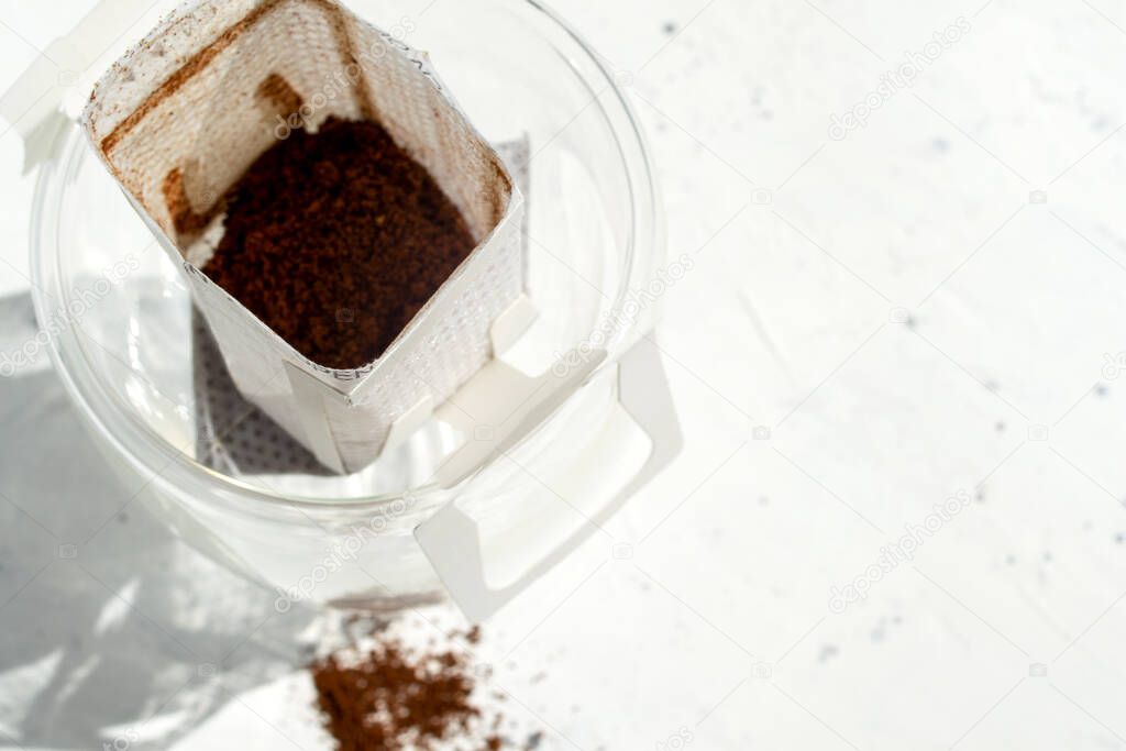 Glass cup with drip coffee bags on white background with copy space. Opened Instant espresso home brew bags still life