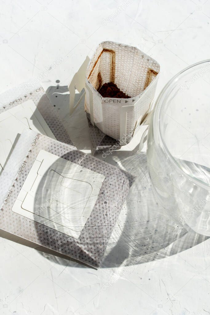 Glass cup with drip coffee bags on white background with copy space. Opened Instant espresso home brew bags still life